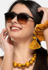 Woman wearing Twig Roth unisex sunglasses with brown gradient lenses and black frame, styled with yellow accessories and summer outfit.