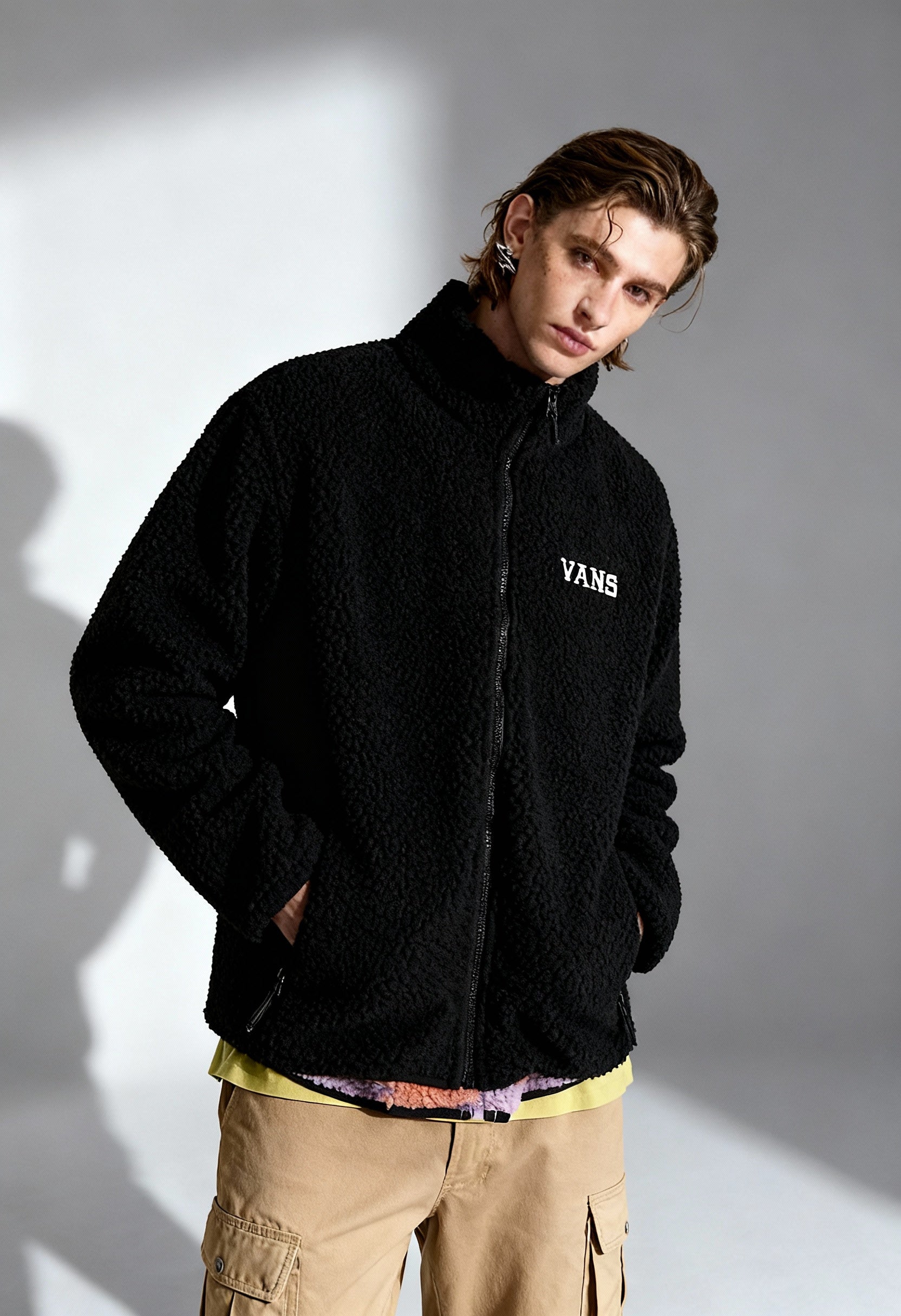 Man wearing Vans VN000NDUBLK1 black fleece zip jacket with visible Vans logo, studio shot.