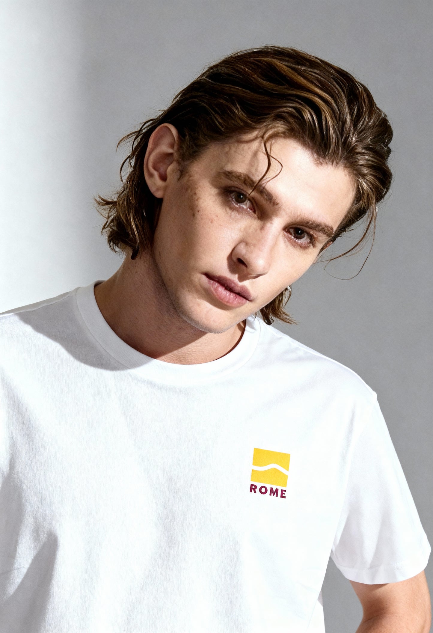 Male model wearing Vans VN0A4CYDWHT1 white cotton T-shirt with yellow front Vans logo, studio shot.
