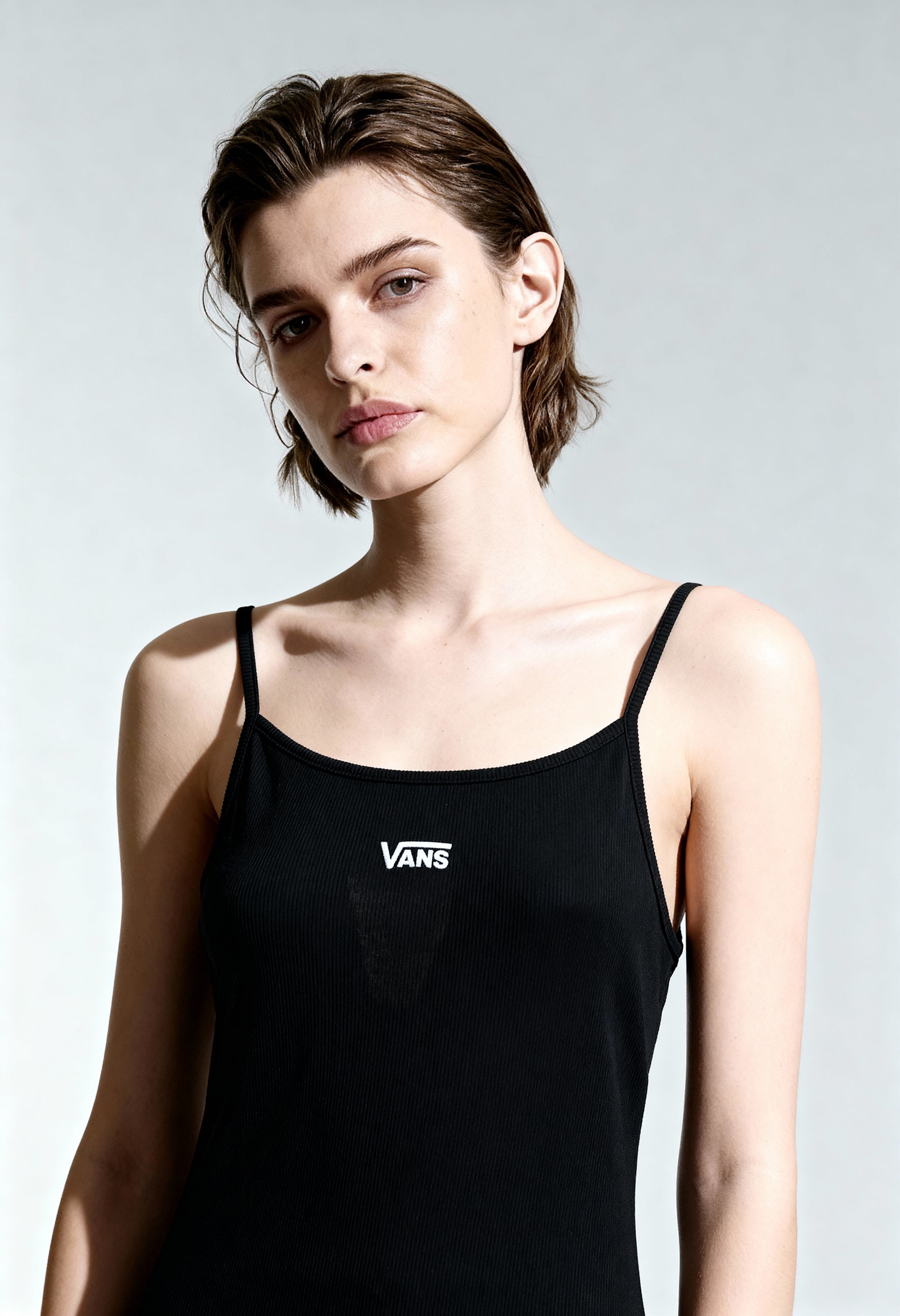 Full-body studio view of woman wearing Vans VN0A5LMEBLK1 black sleeveless mini dress with slim fit.