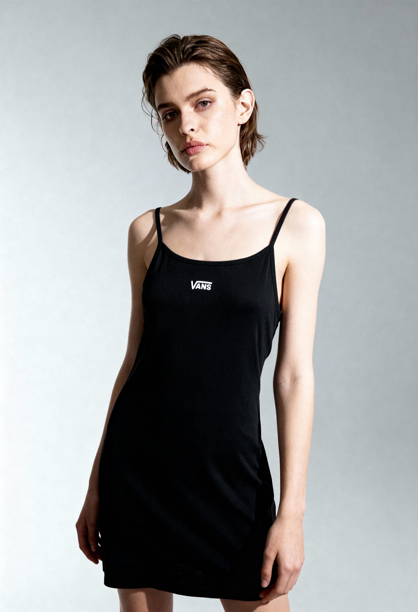Woman wearing Vans VN0A5LMEBLK1 sleeveless black mini dress with visible Vans logo, studio lighting.