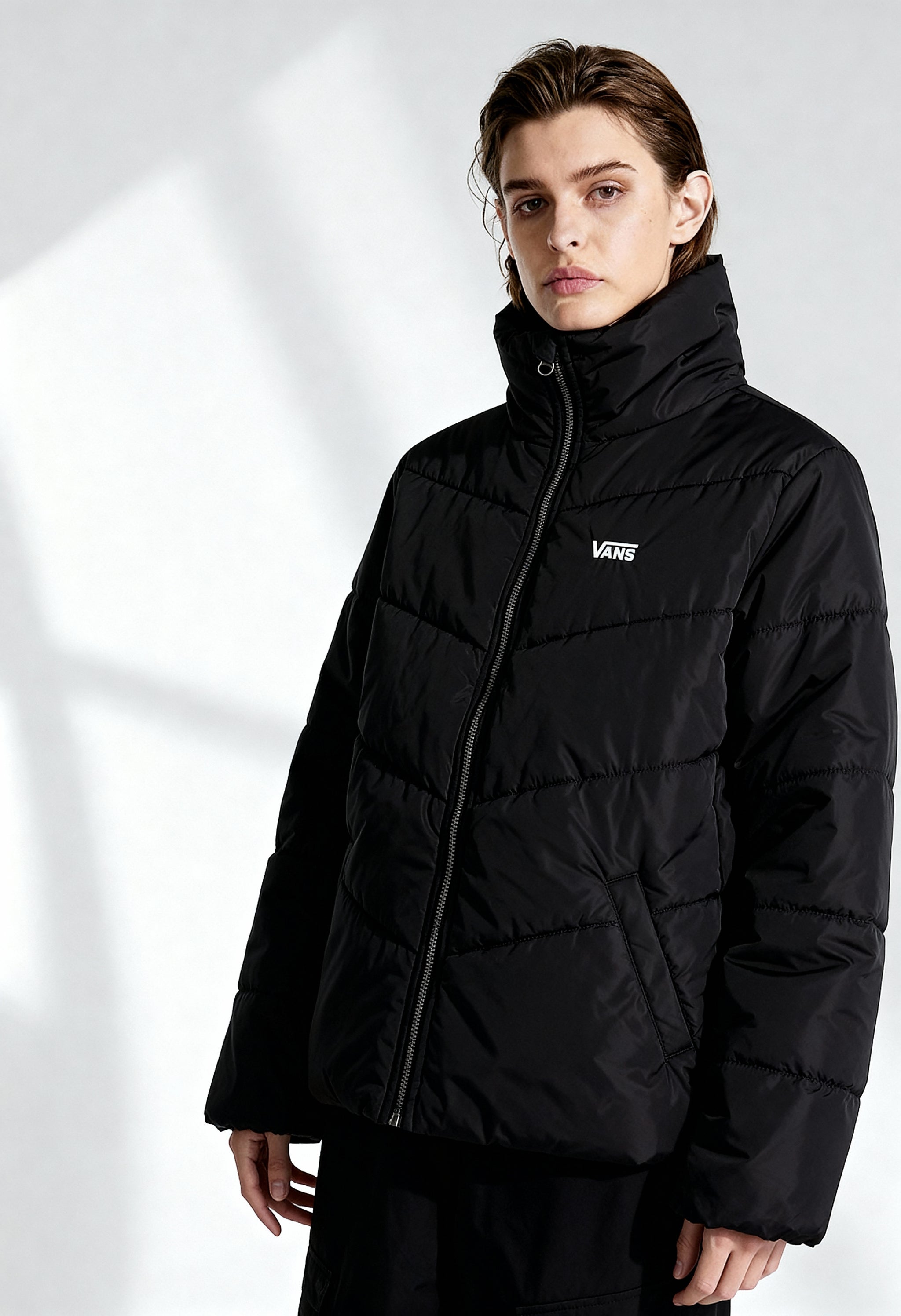 Woman wearing Vans VN0A7YK5BLK1 black bomber jacket with padded design and visible logo, front studio shot.