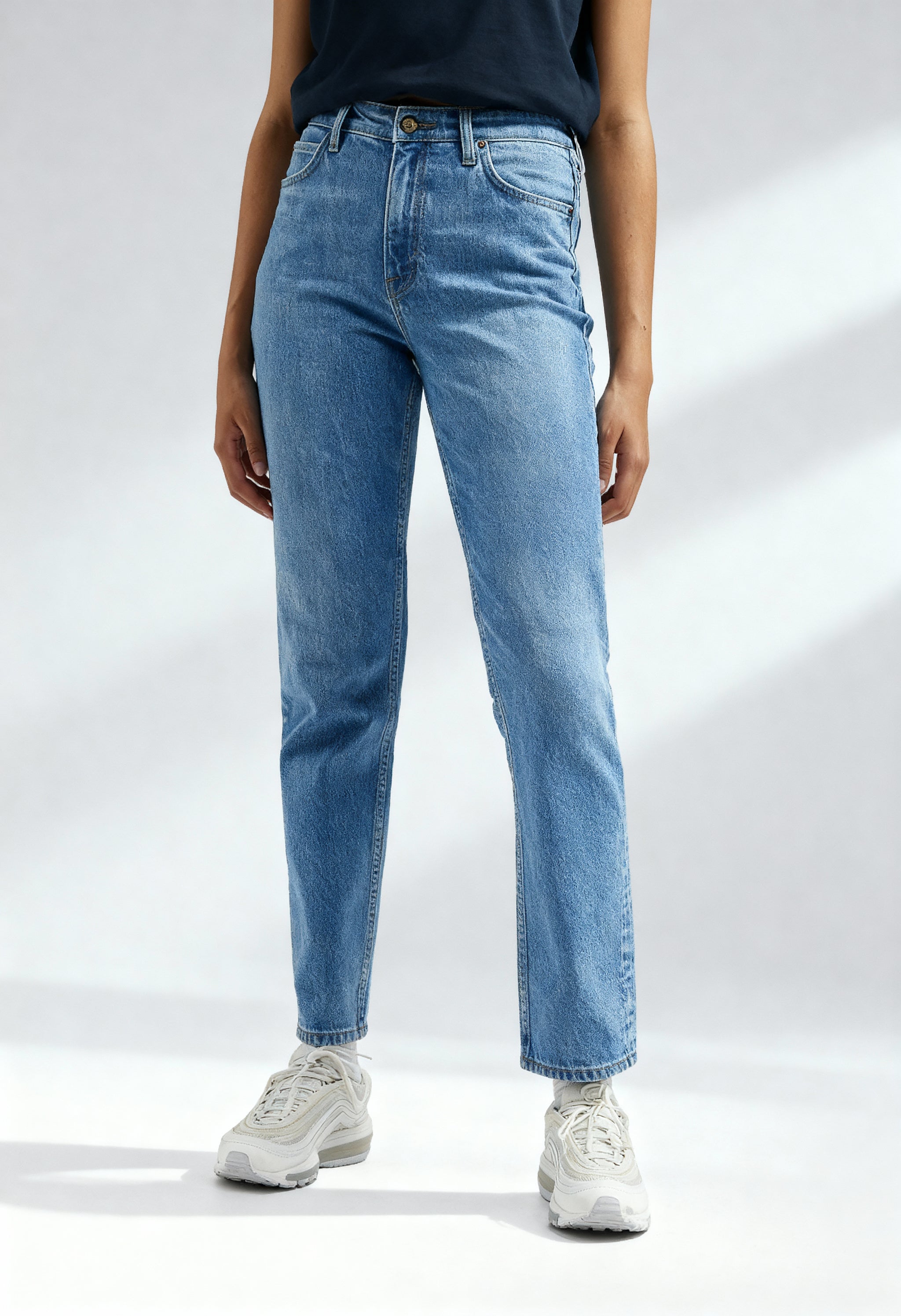Front angled view of a woman wearing light blue Lee L30UOWB59 regular-fit jeans on a bright background.