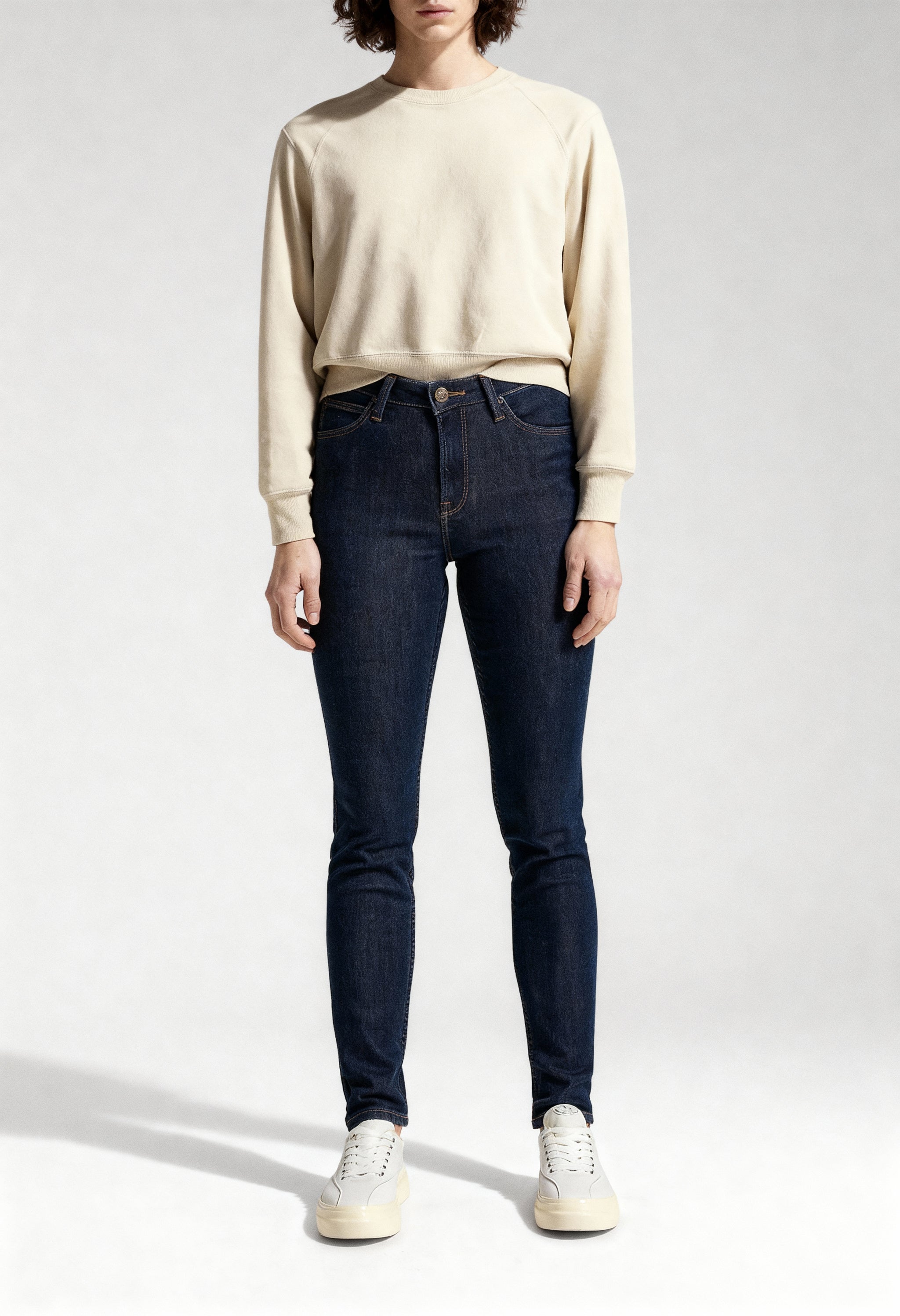Full-length studio shot of a woman wearing dark blue Lee L626MDNX skinny jeans.