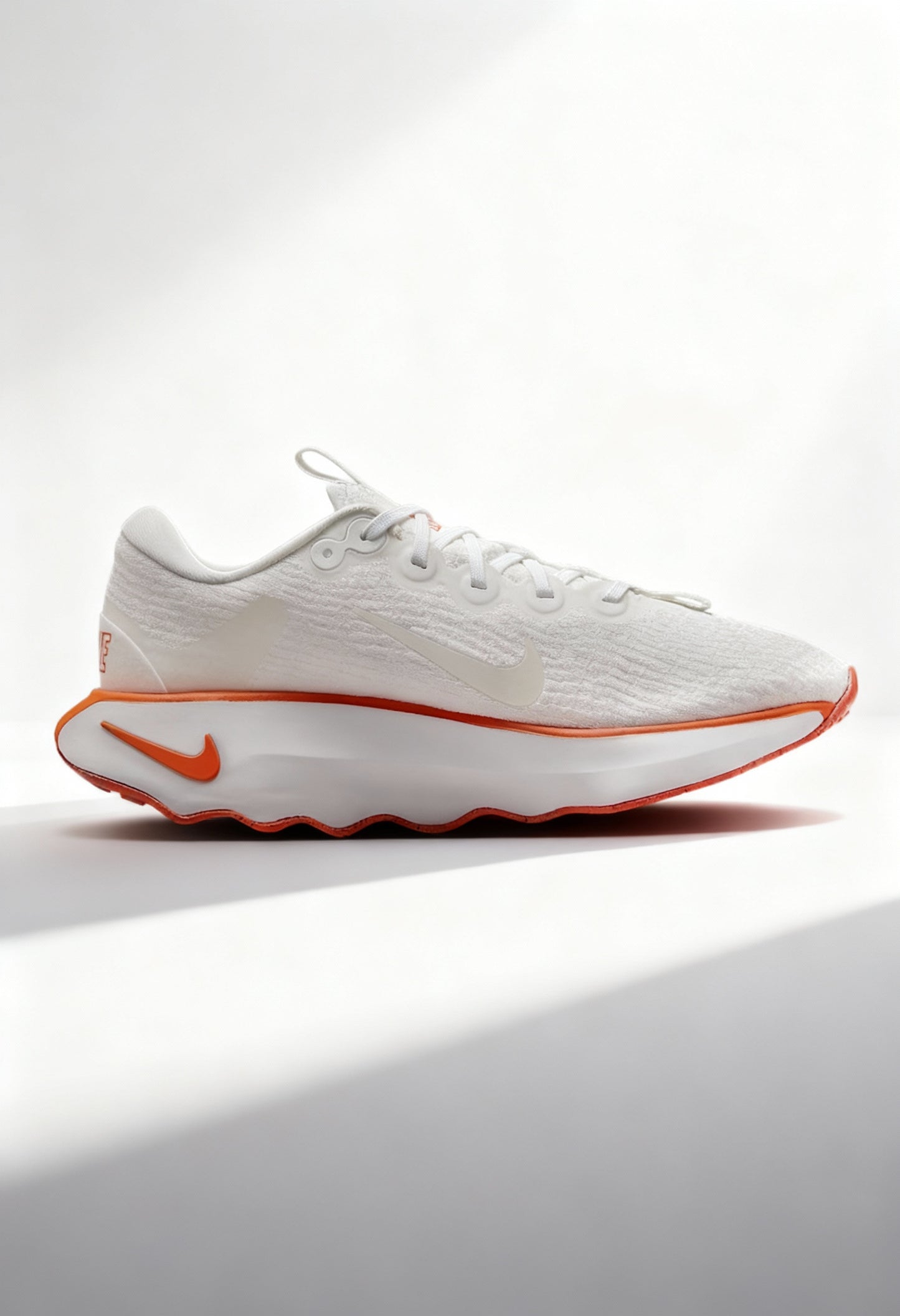 Brand new Nike Motiva women's walking shoes in white and bright orange side view.