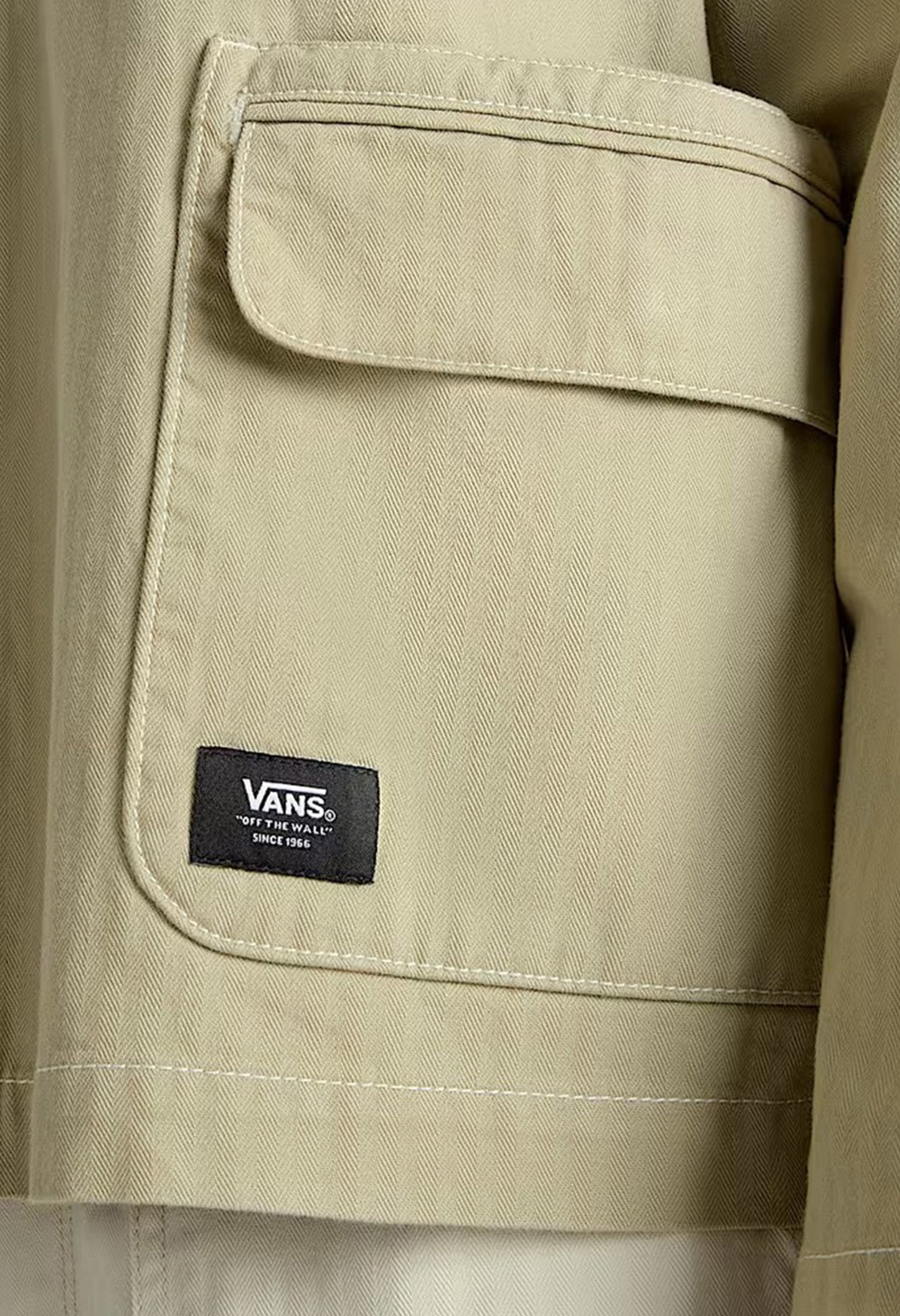Close-up detail of the Vans logo tag on the beige VN000HJRD3Z1 jacket.